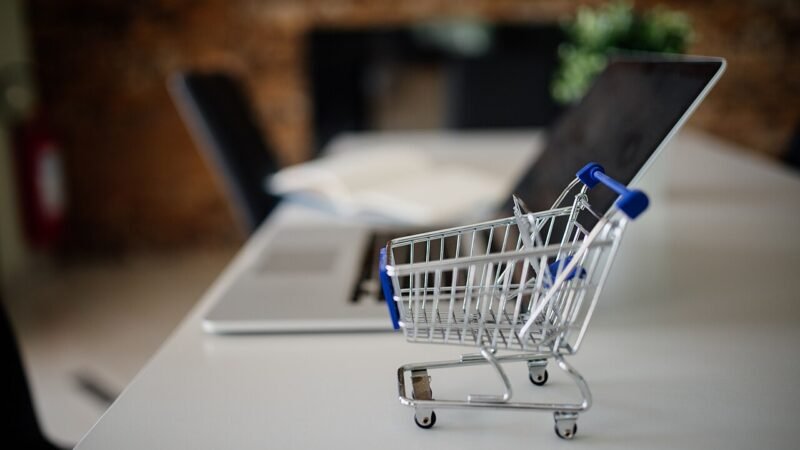 Carrito de compras en miniatura junto a un computador portátil, concepto de comercio electrónico